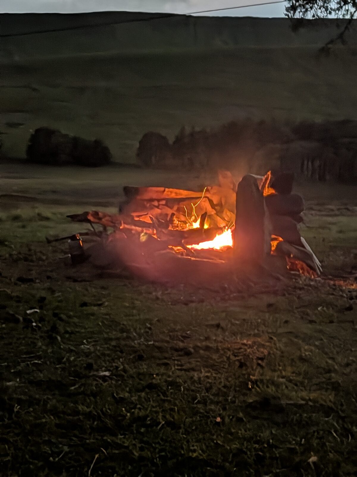 Campfire glowing at dusk in the hills